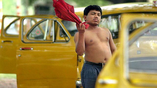 A taxi driver fans himself as a several taxis are parked with doors opened in a street of Kolkata in 2002. AFP