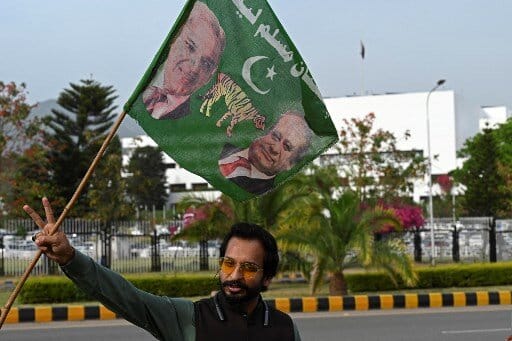 A supporter of Pakistan Muslim League-N (PML-N) holds a party flag with images of Shehbaz Sharif and his elder brother and former prime minister Nawaz Sharif outside the parliament house building in Islamabad on 11 April, 2022. (AFP)
