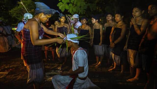 An Indian Rabha tribal girl in traditional attire prepares a Hindu priest before he dances around burning charcoal as part of rituals during Baikho festival