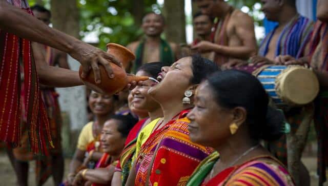 An Indian Rabha tribal Hindu priest serves traditional rice beer to the Rabha women in traditional attire as holy water during Baikho festival