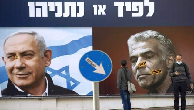 People stand in front of an election campaign billboard for the Likud party showing a portrait of its leader Benjamin Netanyahu, left, and Yair Lapid, in Ramat Gan, Israel. AP