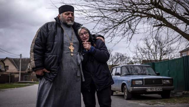 A priest comforts the relative of a deceased civilian man who was exhumed after initially being buried in his yard, in Gostomel village, Kyiv region. AFP