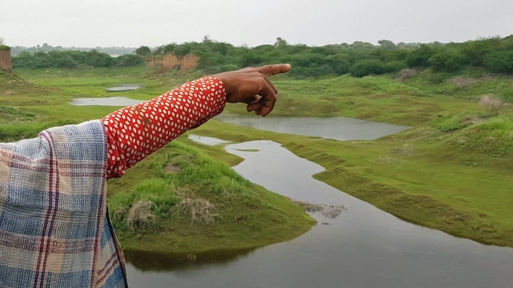 A villager points to land on the banks of the Narmada which was once rich with different crops before it was dug for sand mining. Photo by Hridayesh Joshi.