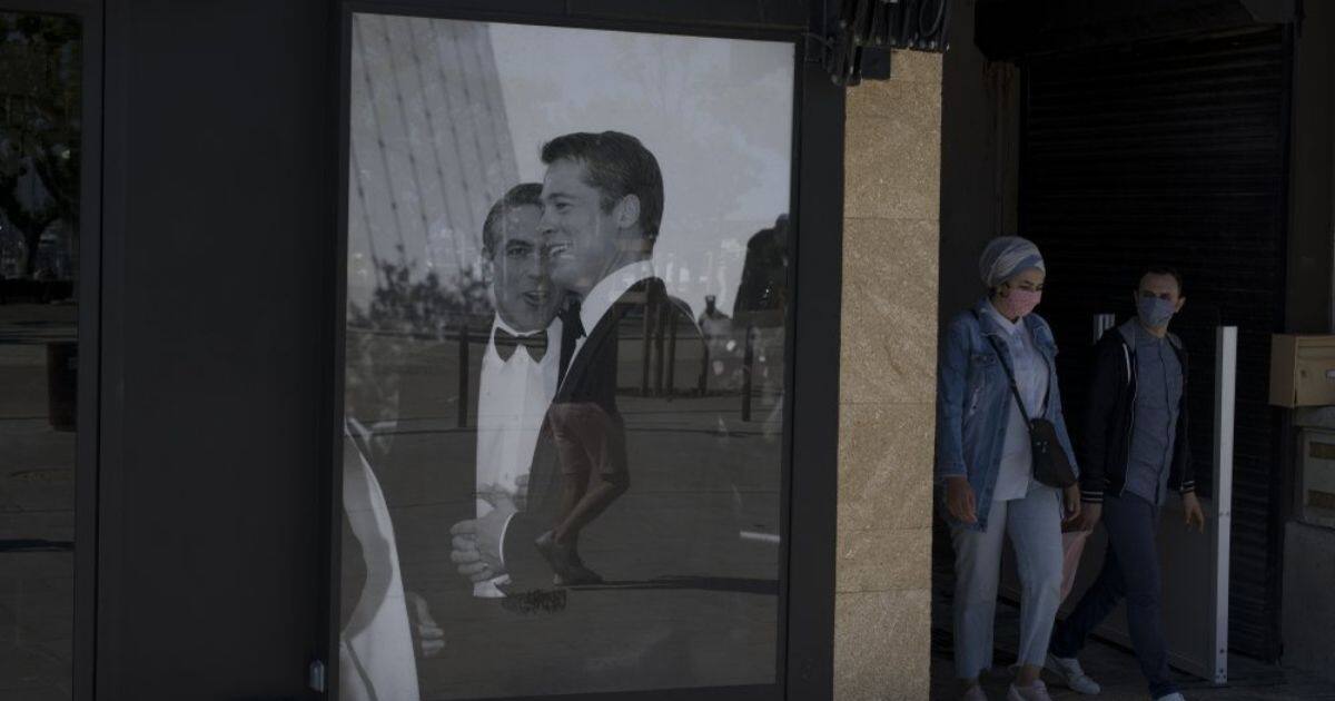 A couple wearing masks to protect from coronavirus walk by a poster of Brad Pitt and George Clooney in Cannes. AP Photo/Daniel Cole